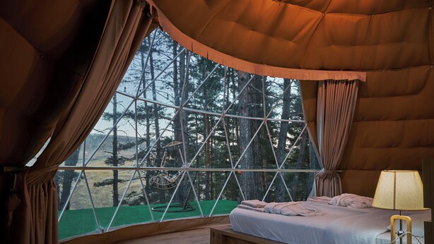 A cozy bedroom with a large window, a bed, and a nightstand with a lamp. - Daxvalley Glamping (Tsalka)