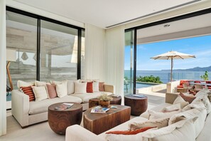 A modern living room with a large sofa, round wooden coffee tables, and a view of the ocean. - Casa Dinamita, a Luxurious Ocean Front Villa with Private Bowling Alley! (Punta Mita)
