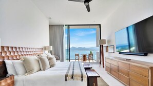 Une chambre d’hôtel moderne dotée d’un grand lit, d’un téléviseur à écran plat, d’une commode en bois et d’un balcon offrant une vue sur les montagnes.