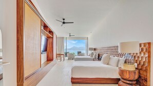 Une chambre d’hôtel moderne avec un grand lit, une tête de lit en bois, un ventilateur de plafond et une vue sur les montagnes par la fenêtre.