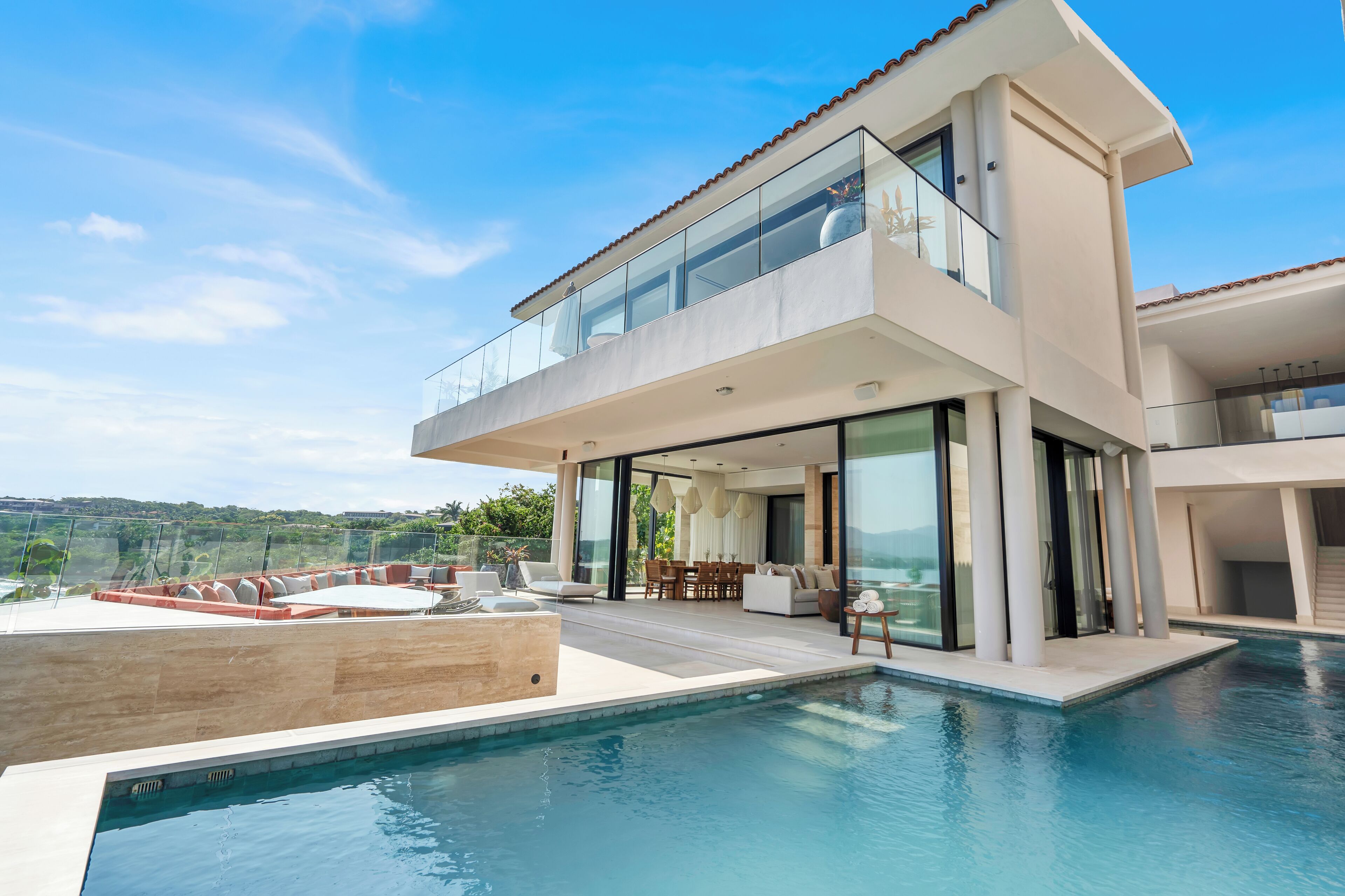 Et moderne hus med to etager, en swimmingpool, store glasvinduer og en patio.