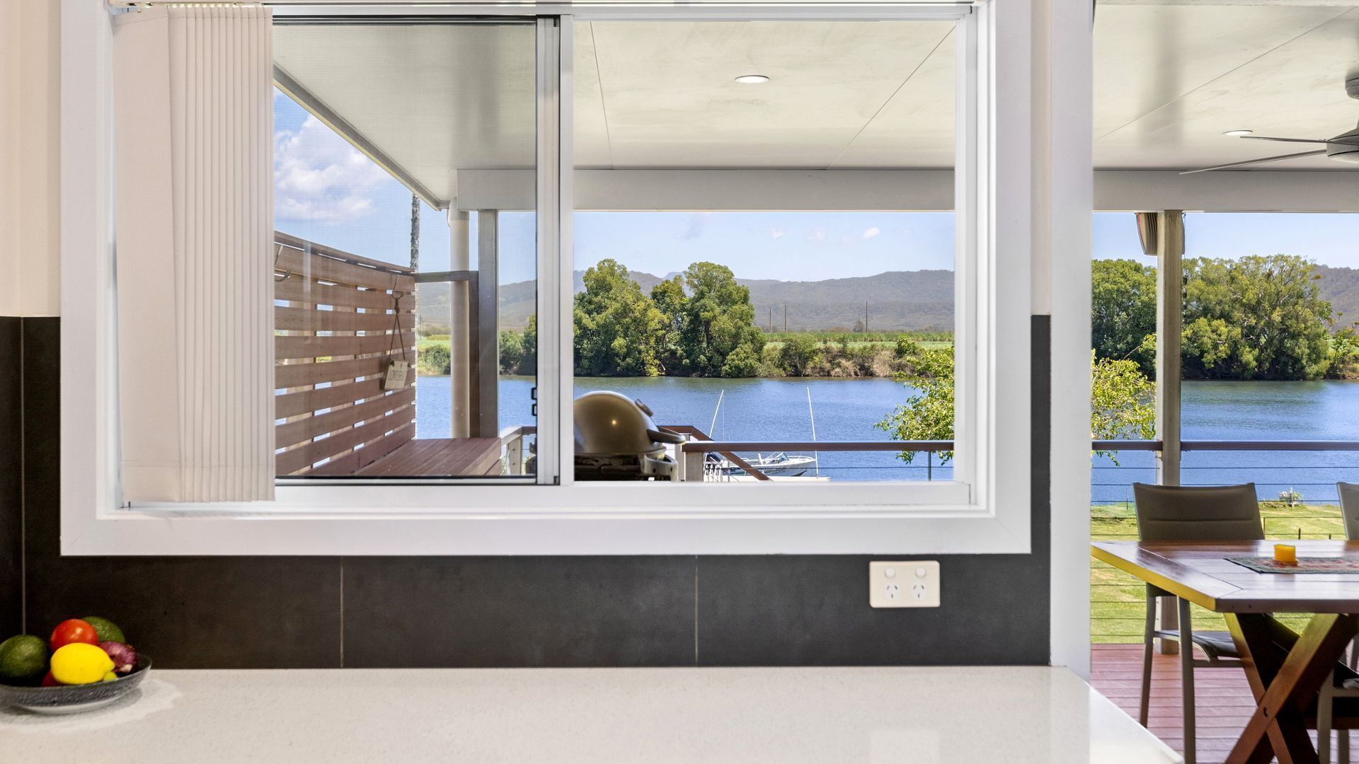 A kitchen with a large window overlooking a lake, a dining area with a table and chairs, and a fruit bowl on the counter.