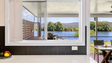 A kitchen with a large window overlooking a lake, a dining area with a table and chairs, and a fruit bowl on the counter.