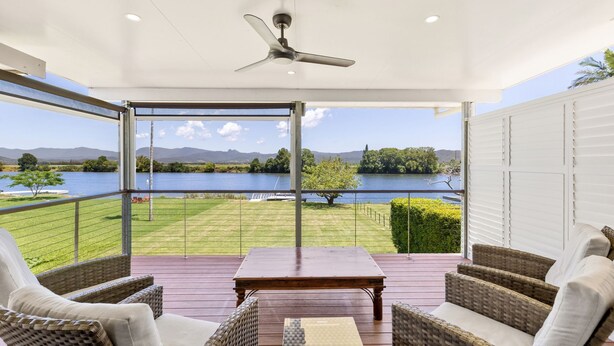 Una terraza techada al aire libre con mobiliario de mimbre, una mesa y vistas a un lago y montañas.