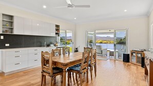 Una cocina moderna con armarios blancos, una mesa de comedor de madera y sillas. Se ve un lago y montañas a través de puertas correderas de vidrio.