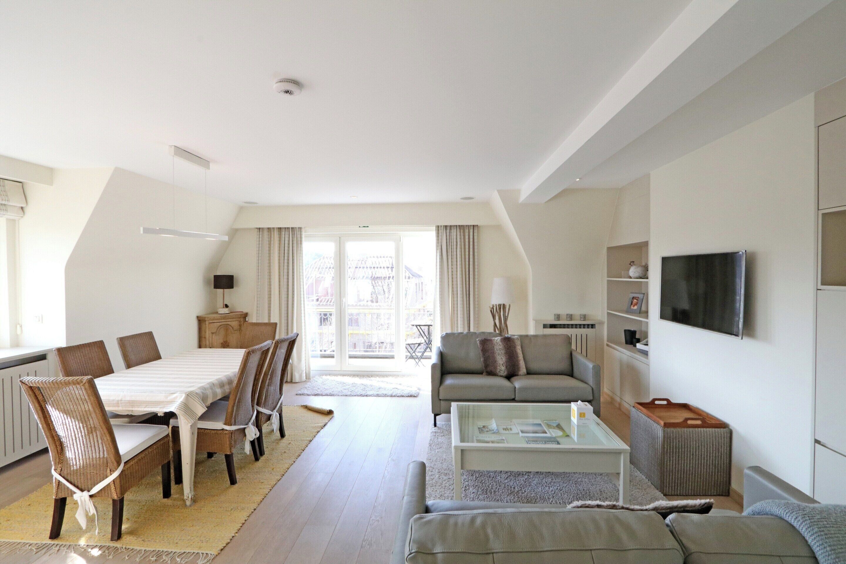 A modern living room with a dining area, a sofa, a coffee table, and a television.