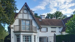 Una casa de dos pisos con balcón, un patio con mobiliario exterior y un jardín bien cuidado.