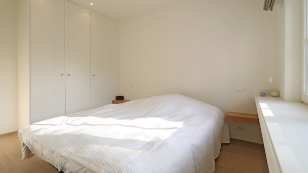 Un dormitorio con una cama grande, un armario, una mesita de noche y una ventana.