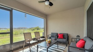 Una habitación amplia con ventanas grandes, ventilador de techo, sofá, mesa y dos sillas.