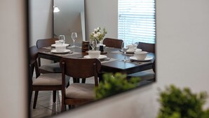 Un comedor con una mesa dispuesta para cuatro personas, incluyendo copas de vino, platos y un florero con flores.