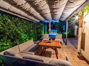An outdoor patio with a covered seating area, a wooden table, and a hot tub. - Two-Bedroom Holiday Home With Pool (Brodarica)