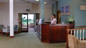 A reception area with a wooden reception desk, a seating area with chairs, and a view of the outdoors through a glass door.