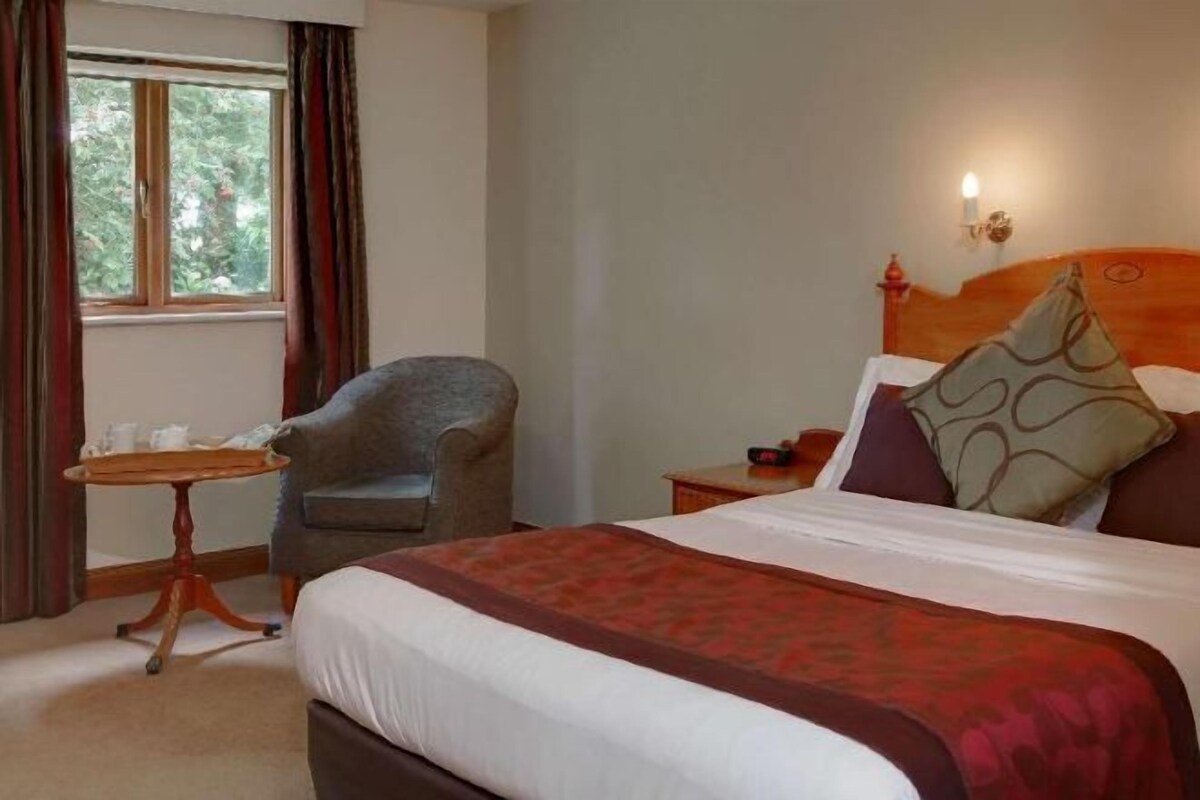 A hotel room with a bed, a chair, a small table, and a window.
