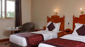 A hotel room with two beds, a desk, a chair, and a window.