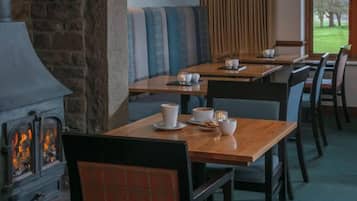 Un restaurante con mesas y sillas de madera, una chimenea de piedra y vistas al exterior.