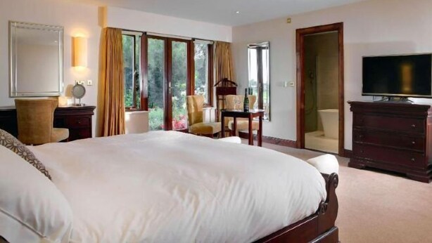 A hotel room with a large bed, a television, a desk with a chair, and a wardrobe.