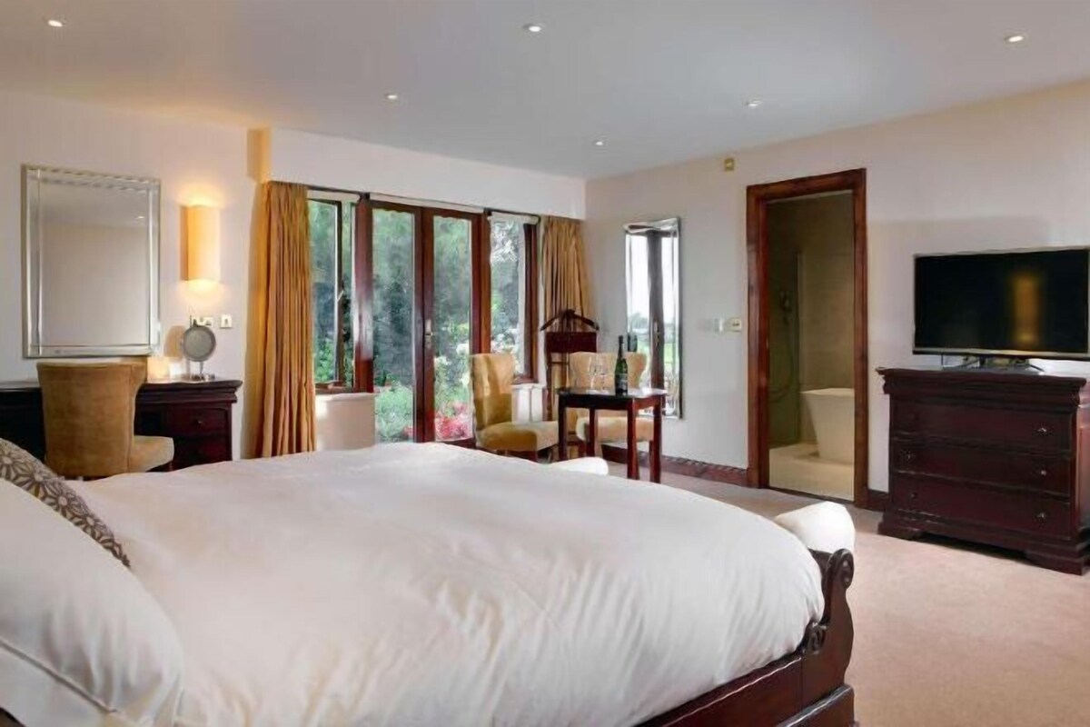 A hotel room with a large bed, a television, a desk with a chair, and a wardrobe.