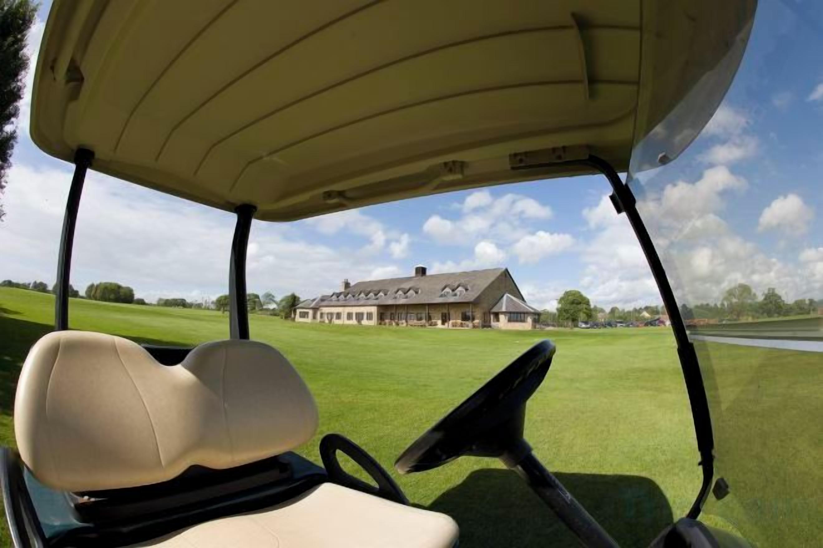 A golf cart interior with a view of a golf course and a building in the distance.