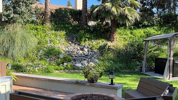 A garden with a stone wall, a pergola, and a fire pit area. - Oceanside tranquility (Oceanside)