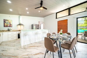 A modern kitchen with white cabinets, a marble floor, and a dining area with a glass table and brown chairs.