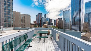 Eine Dachterrasse mit Tisch und Bänken, mit Blick auf einen Stadtblick mit modernen Gebäuden.
