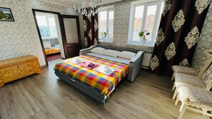 Une chambre d’hôtel avec un grand lit, une commode en bois, une chaise et une fenêtre avec des rideaux.