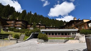 A hotel with multiple balconies, a central building with large windows, and a mountainous backdrop. - Presanella Alpine Apartment Mhd (Madonna di Campiglio)