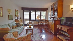 A cozy living room with a sofa, armchairs, a coffee table, a TV, and a dining area with a table and chairs. - Presanella Alpine Apartment Mhd (Madonna di Campiglio)