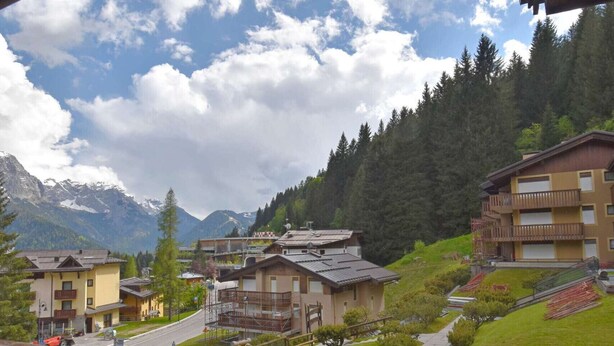 A view of a mountain town with buildings, a pathway, and benches. - Presanella Alpine Apartment Mhd (Madonna di Campiglio)