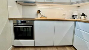 Una cocina moderna con armarios blancos, horno empotrado, cafetera y encimera de madera.