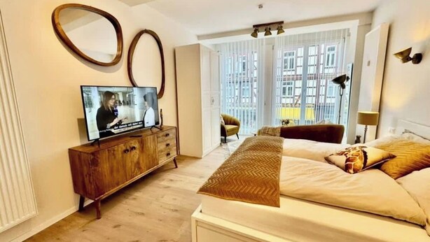 Un dormitorio con cama, un televisor sobre un mueble de madera y vistas al exterior a través de amplios ventanales.