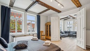 A spacious room with a large bed, a wooden chair, a cabinet, and a view of the outside. - MEL&BENS Rathaus-Suite | old town | park option (Celle)