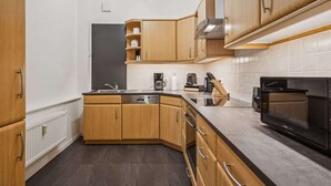 A modern kitchen with wooden cabinets, a dishwasher, a stove, and a microwave. - MEL&BENS Rathaus-Suite | old town | park option (Celle)