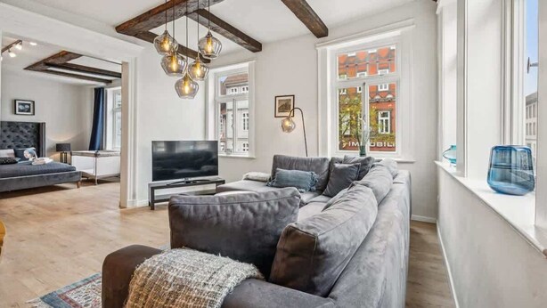 A modern living room with a sectional sofa, a flat-screen TV, and exposed wooden beams. - MEL&BENS Rathaus-Suite | old town | park option (Celle)