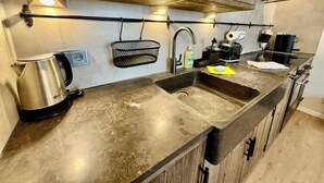 Eine Küche mit Spüle aus Edelstahl, einem Wasserkocher, einer Kaffeemaschine und Holzschränken.