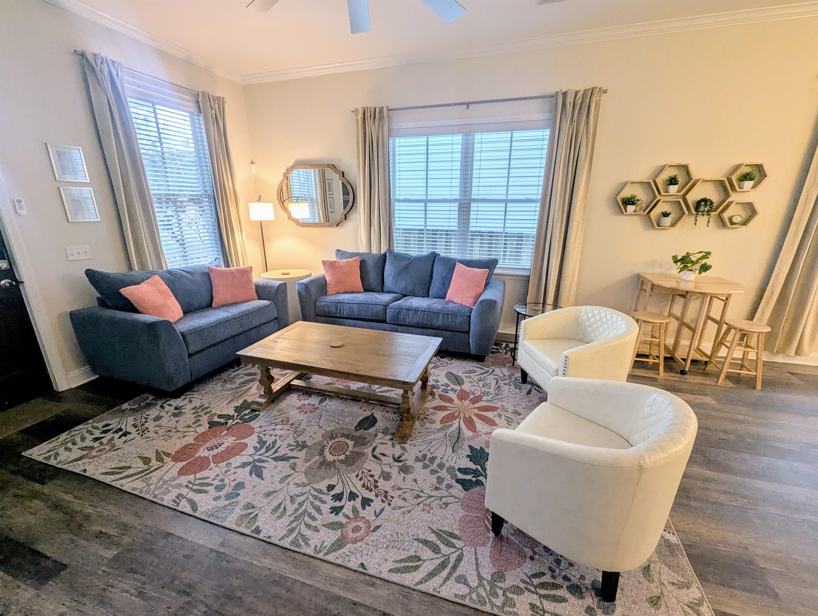 A living room with a sofa set, a coffee table, a white armchair, a small round table with chairs, and a decorative wall piece.