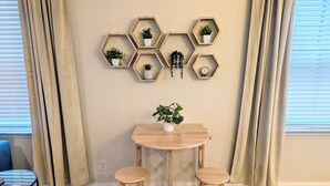 Una habitación con un adorno hexagonal en la pared, una mesa redonda de madera, dos taburetes de madera, una silla azul y una alfombra estampada.