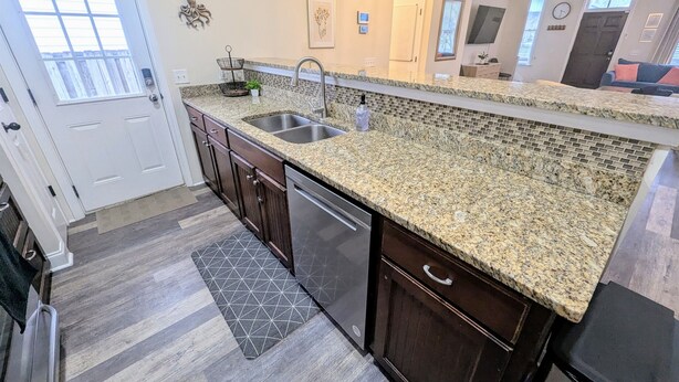 Una cocina con armarios de madera oscura, encimeras de granito, un lavabo doble y un lavavajillas.