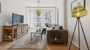 Una sala de estar con sofá, mesa de centro, televisor, aparador de madera y lámpara de pie.
