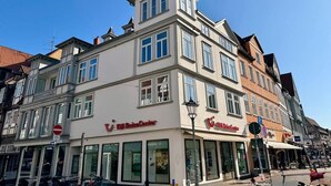 Un edificio de varios pisos con locales comerciales en la planta baja, incluyendo un escaparate visible con letreros.