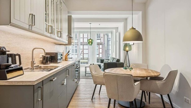 Cocina moderna con comedor, que incluye una isla grande, electrodomésticos integrados y una lámpara colgante.