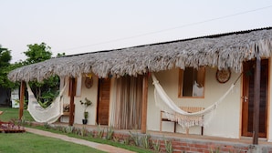 A thatched-roof house with a porch, a hammock, and a small garden. - Vila Orun - Guest house (Barreirinhas)