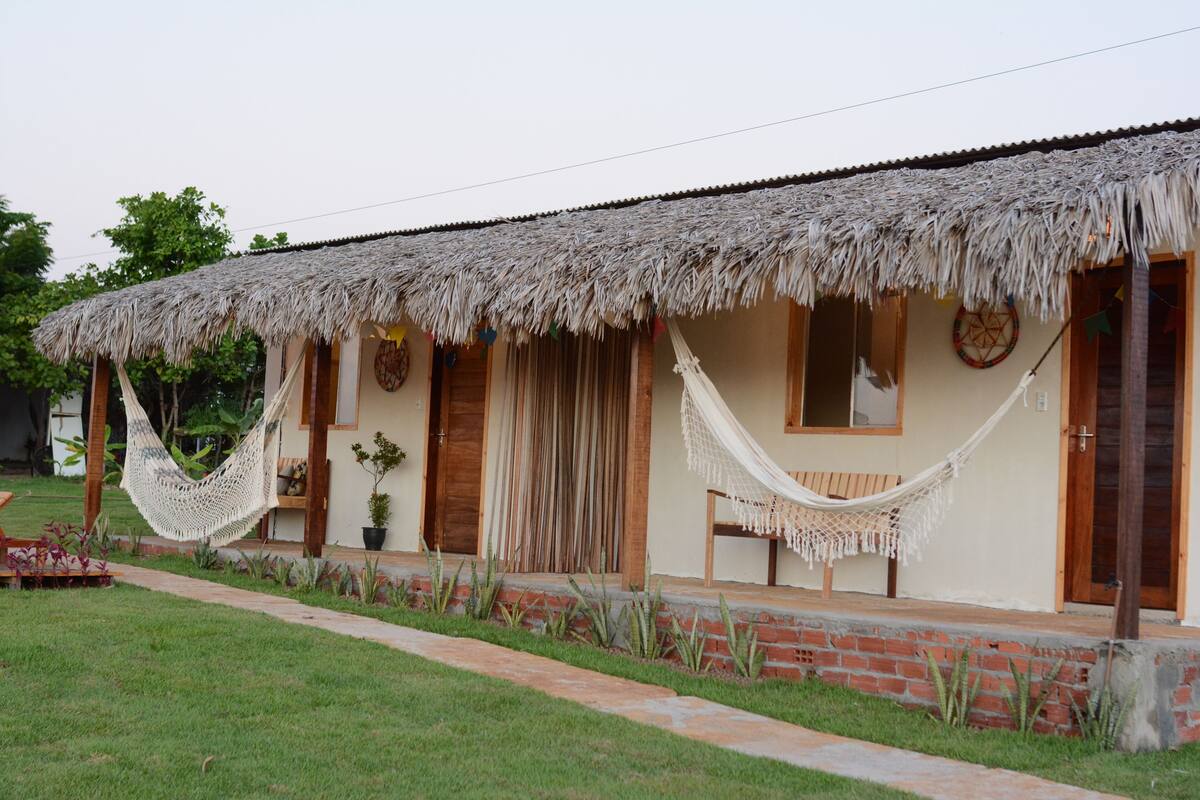 A thatched-roof house with a porch, a hammock, and a small garden.