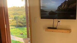 A room with a television mounted on a wall, a wooden shelf below it, and a white cabinet to the right. - Vila Orun - Guest house (Barreirinhas)