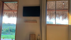 A bedroom with a bed, a TV mounted on the wall, and a window with curtains. - Vila Orun - Guest house (Barreirinhas)