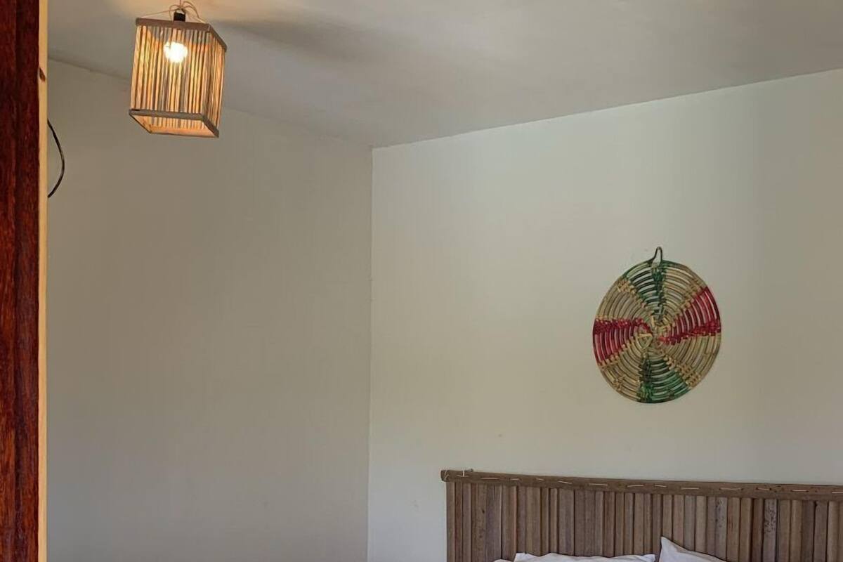 A neatly made bed with white linens, a wooden headboard, and a wall-mounted decorative item.