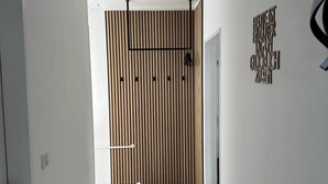 Een gang met een wand van houten latten, een zwart metalen rek en een hangend klokje.