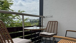 Een balkon met rieten stoelen en een houten tafel, een glas water en uitzicht op groen.