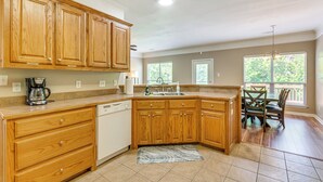 A kitchen with wooden cabinets, a dishwasher, a coffee maker, and a dining area with a table and chairs. - 11 Mi to Dtwn Little Rock: Home w/ Large Deck! (Mabelvale)