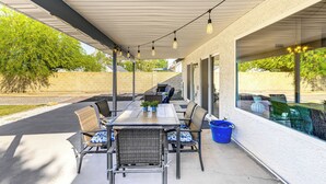 An outdoor patio with a table and chairs, string lights, and a blue bucket.